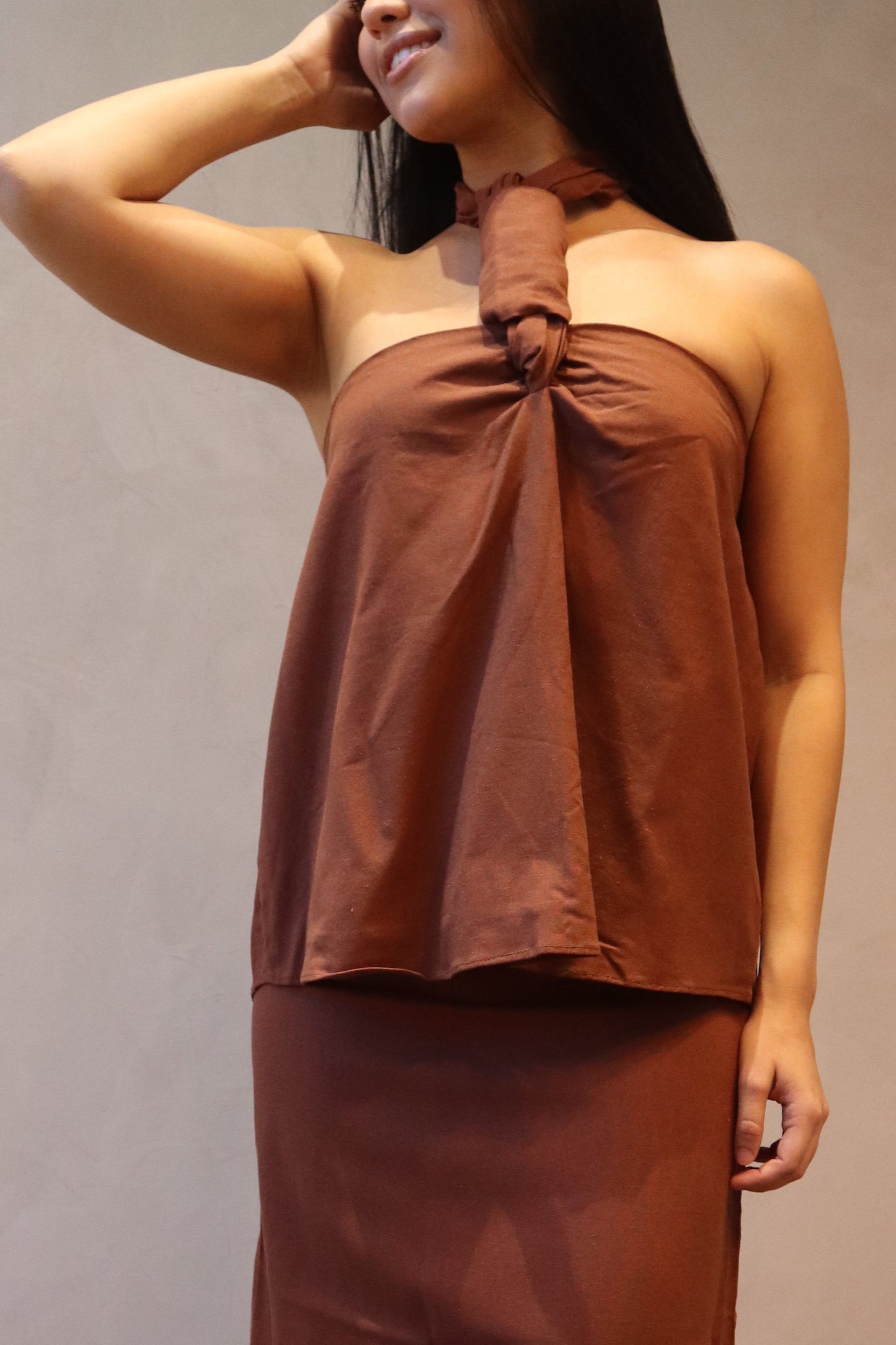 Woman in a brown dress standing in a room with wooden floor and beige walls.