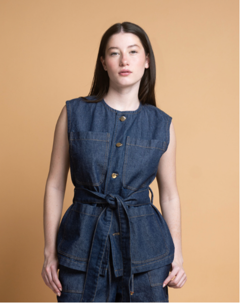 Woman wearing a denim vest over a dress against a beige background